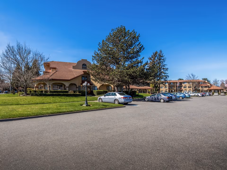 Exterior view of Holiday Redwood senior living facility with parking lot and trees.