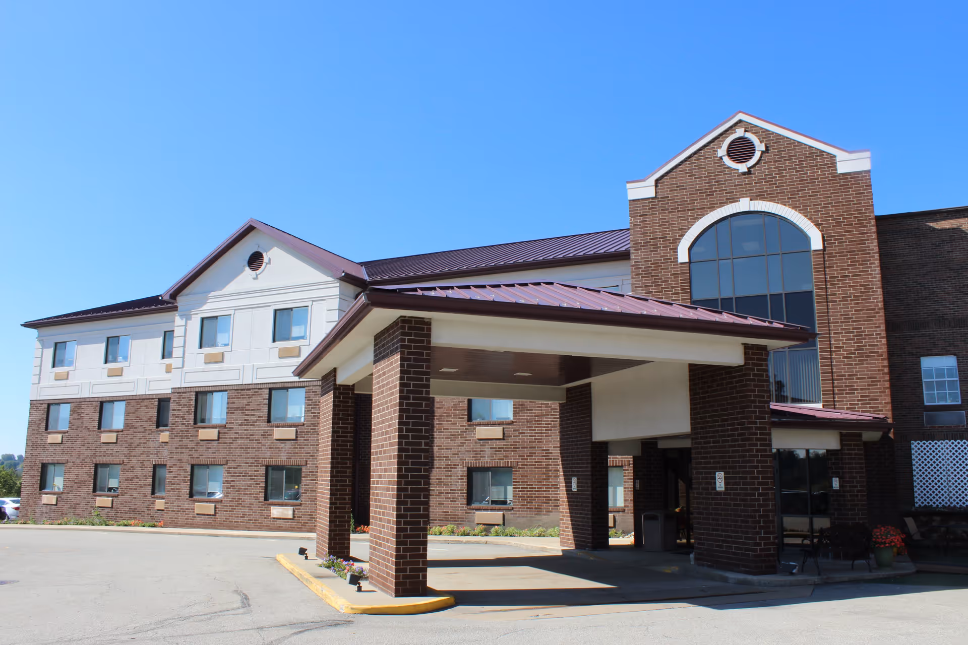 Front entrance of a brick nursing and rehabilitation center with a covered drop-off canopy and multiple windows under a clear blue sky.