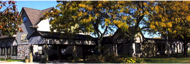 Exterior view of a large residential-style building partially shaded by trees with autumn foliage under a clear blue sky.