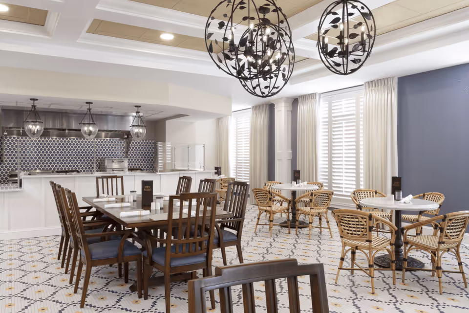 Spacious dining room with wooden and wicker tables and chairs, patterned tile floor, decorative pendant lights, and an open kitchen counter.