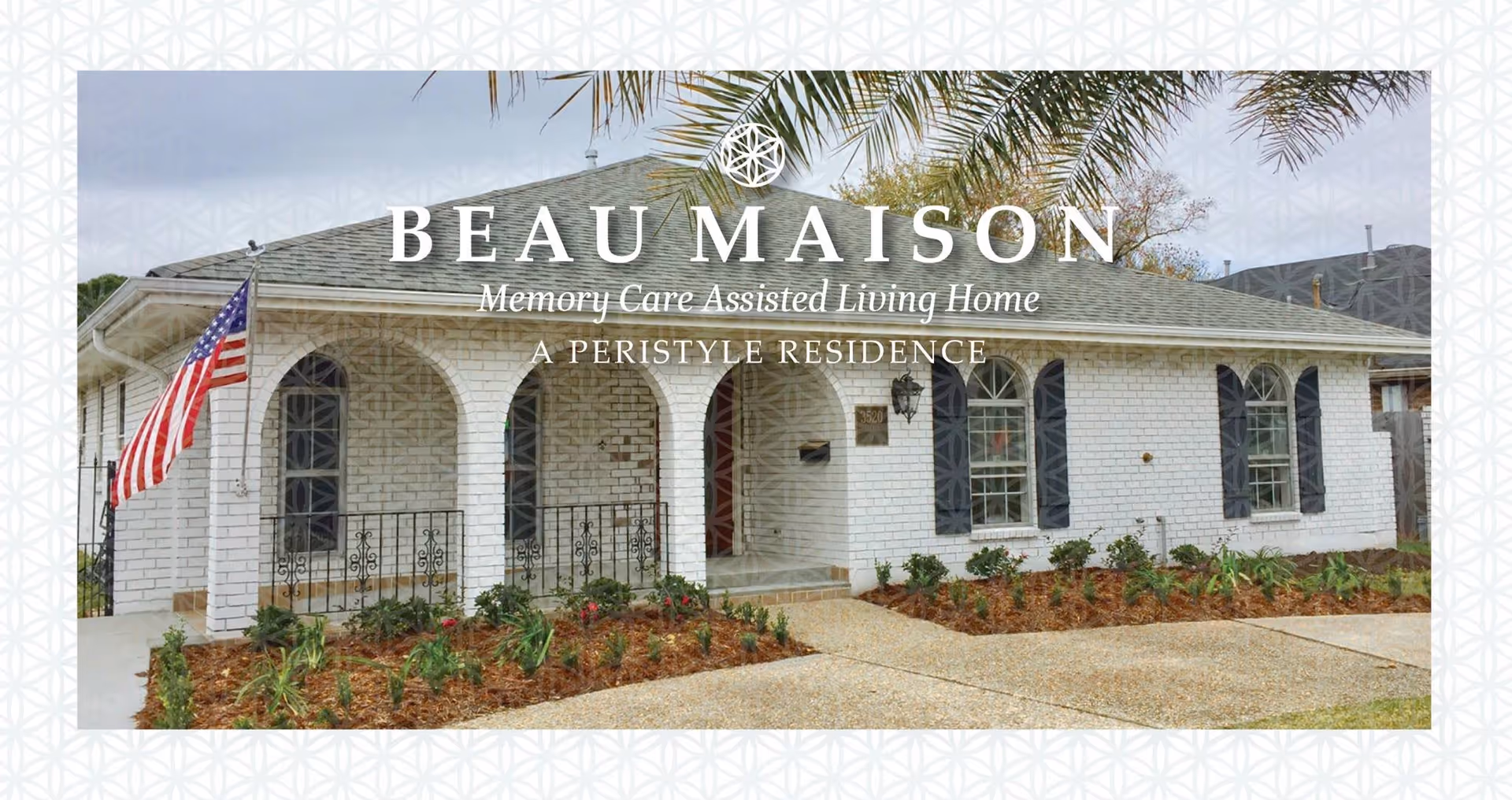 Exterior view of a single-story white brick building with arched windows and a covered porch. There is an American flag on a pole near the entrance, and landscaping with plants and mulch in front of the building. The sky is overcast.