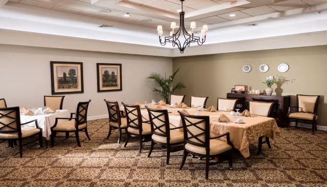 A formal dining room with two tables set for service, cushioned chairs, a chandelier, sideboard and wall decor.
