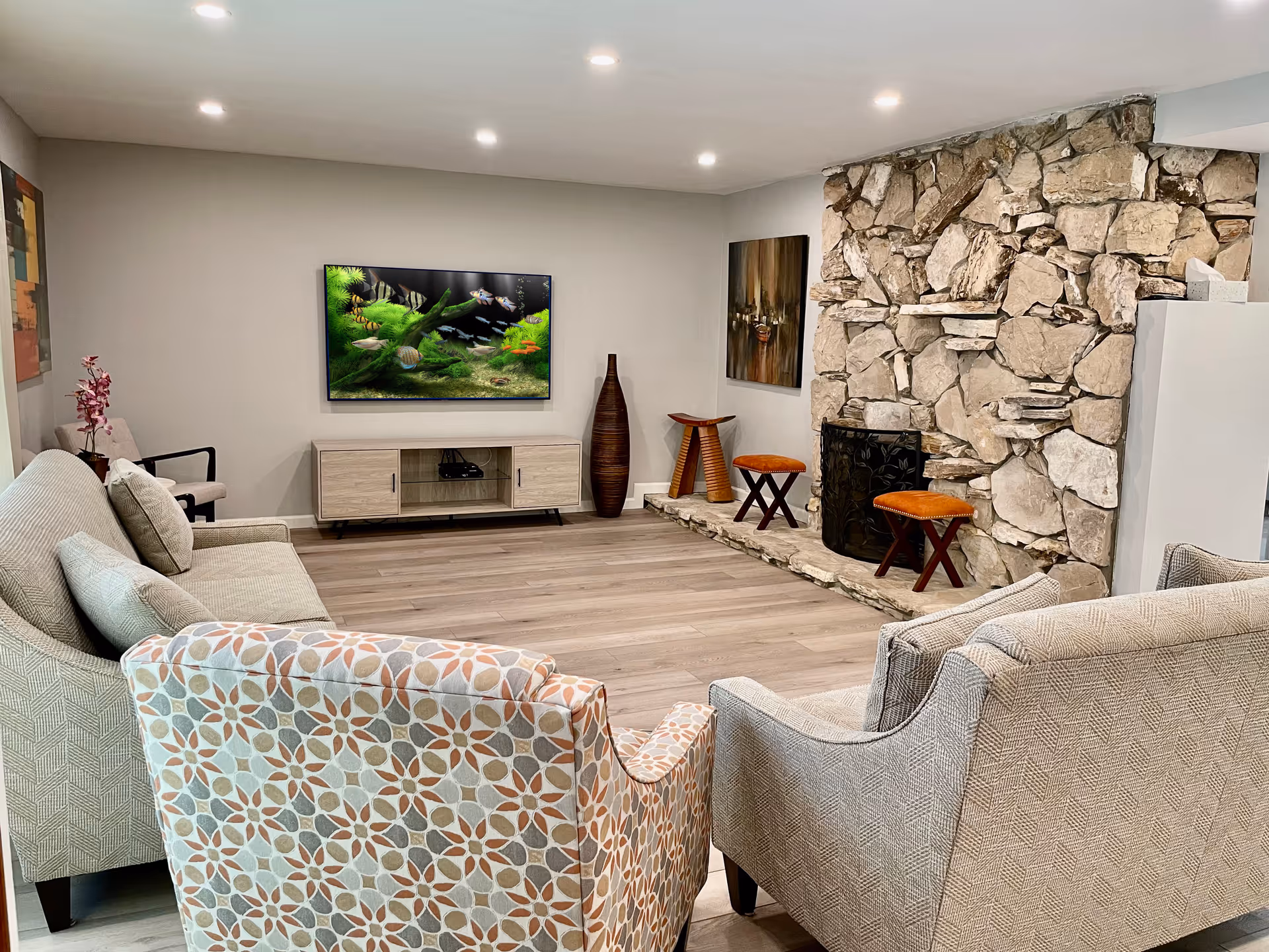 Bright living room with patterned and neutral sofas facing a wall-mounted TV and a large stone fireplace.