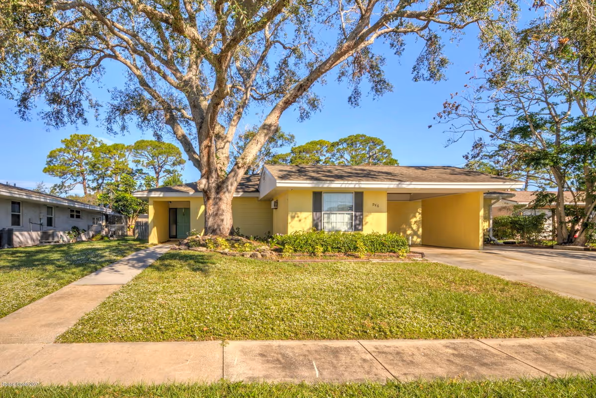 A single-story yellow assisted living building with a large front yard and driveway.