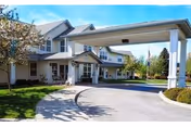 Front entrance of a two-story senior living facility with a porte-cochere, driveway, landscaping and an American flag.