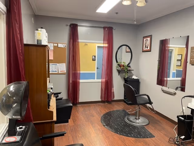 Small hair salon interior with a styling chair, mirror, hair-drying station, and wood-look flooring.