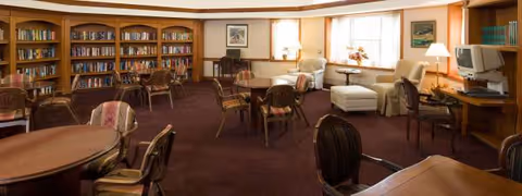 Senior living common area with bookshelves, couches, and desks in a warm, well-lit room.