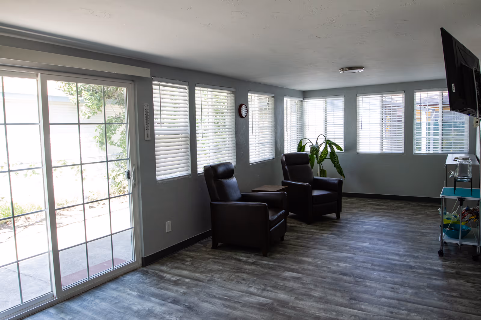 Bright common room with two leather armchairs, a small table, large sliding glass doors and multiple windows.