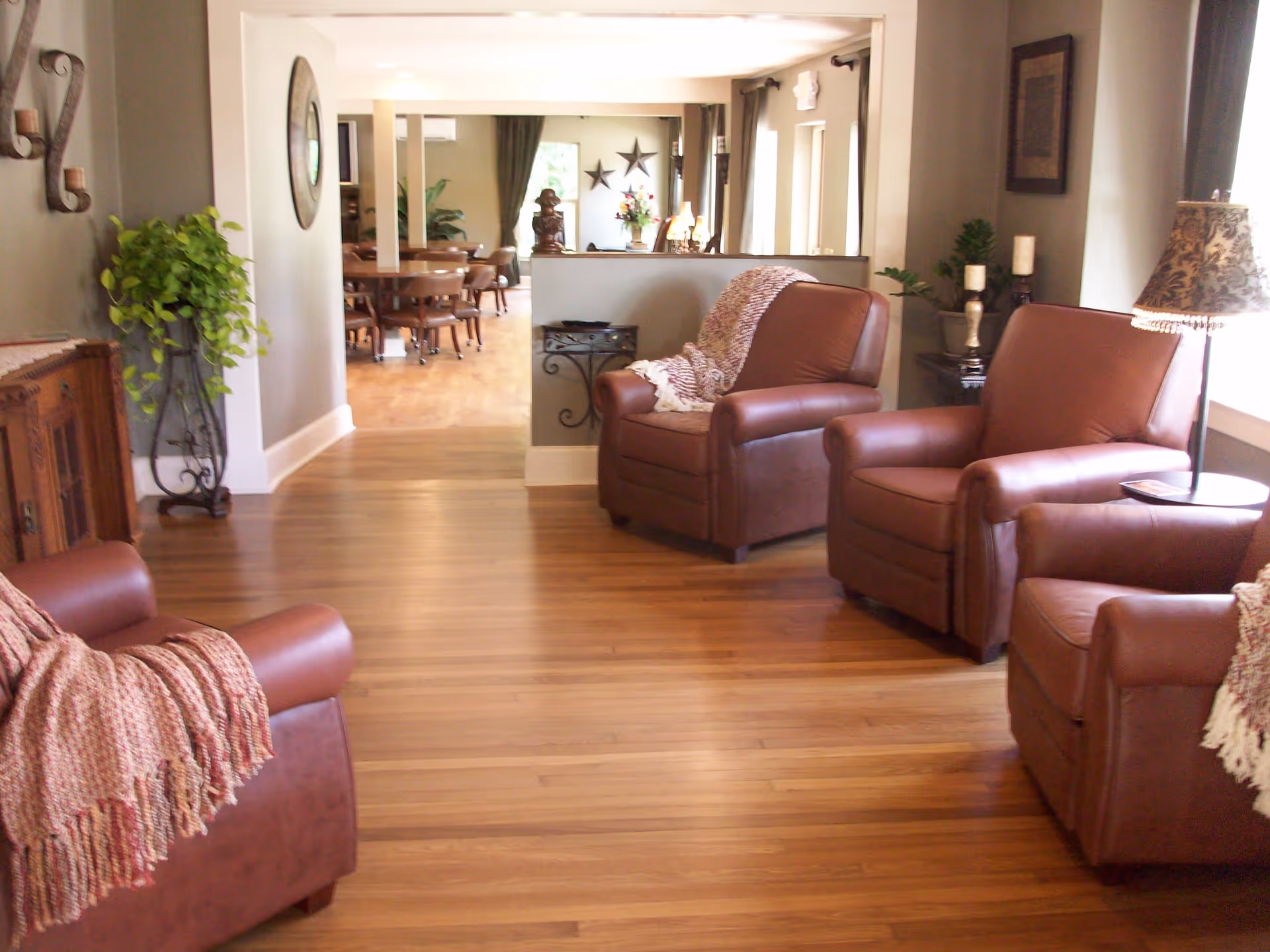 Sunny living room with leather armchairs and hardwood floors opening into a dining area.