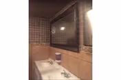 Interior view of a bathroom with a double sink vanity, a large rectangular mirror with a dark frame above the sinks, brown tiled walls, and a soap dispenser mounted on the wall.