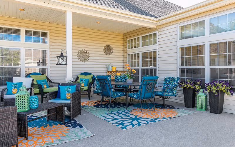 Covered outdoor patio with colorful wicker seating, a dining table, patterned rugs, and potted plants.