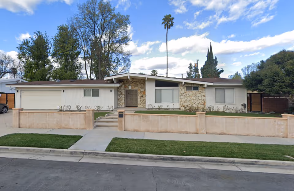 Single-story senior living facility with stone facade, low wall, and a manicured front yard.