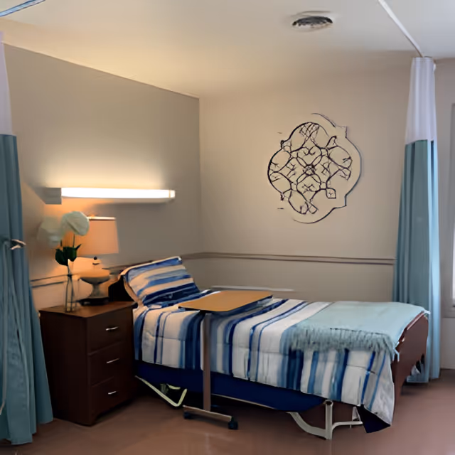 A neatly made single bed with blue and white striped bedding in a room. Next to the bed is a wooden nightstand with a lamp and a vase with white flowers. A wall-mounted light fixture is above the nightstand. There is a decorative wall art piece above the bed. Light blue curtains hang on either side of the room.