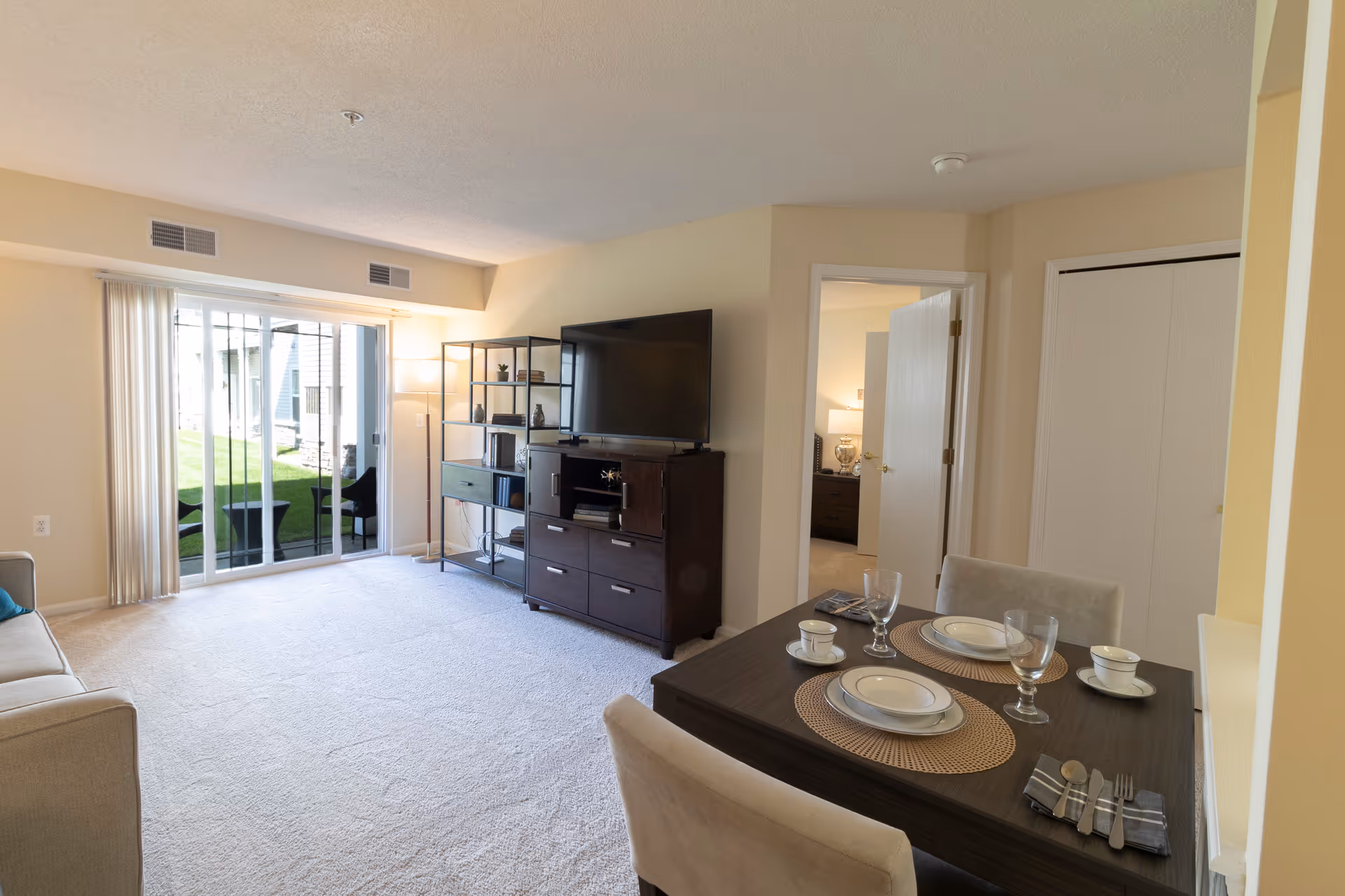 Spacious living room with a TV and shelving, sliding glass patio doors, and a small dining table set.