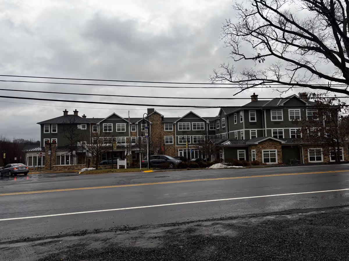 Front exterior of a three-story assisted living building by a wet road on an overcast day.