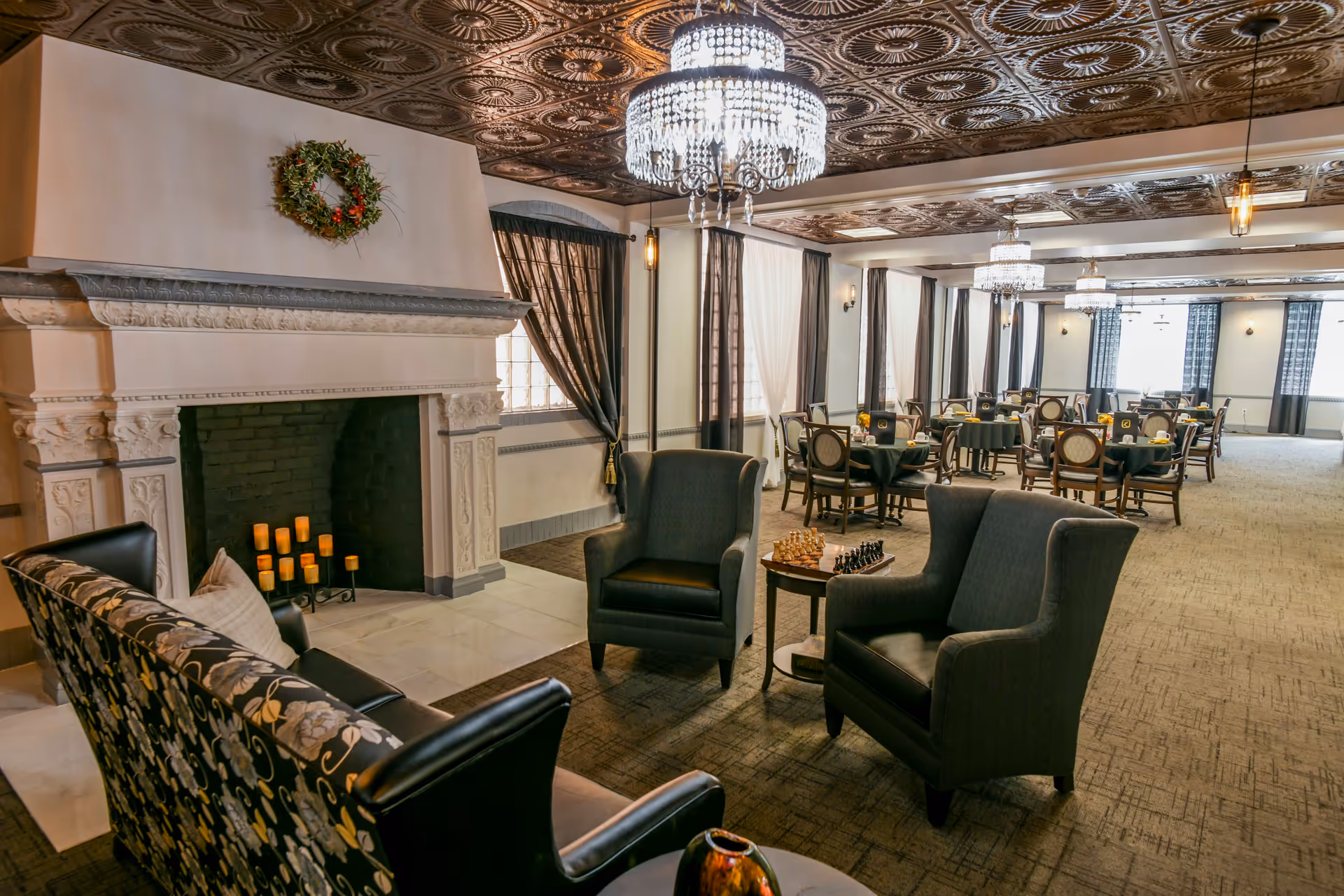 Spacious elegant dining and lounge area with a fireplace, chandeliers, armchairs, and multiple dining tables.