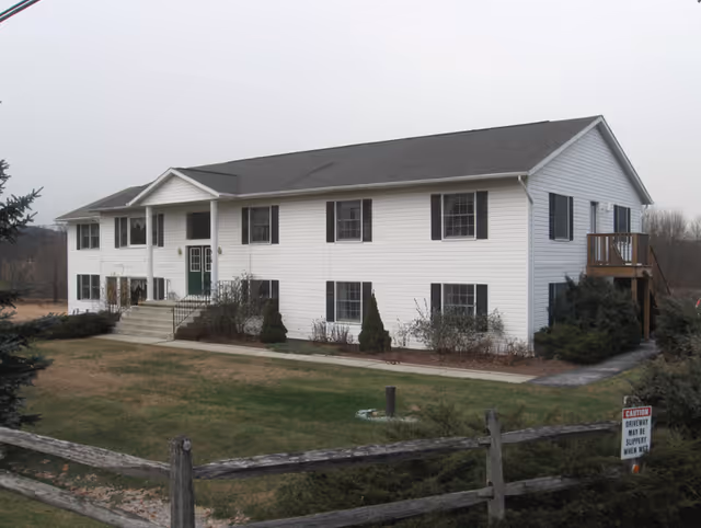 Front view of a two-story white siding residential building with black shutters, a small porch, and a lawn.