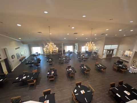 Spacious dining room with multiple tables covered in black tablecloths, chandeliers, and wood flooring.