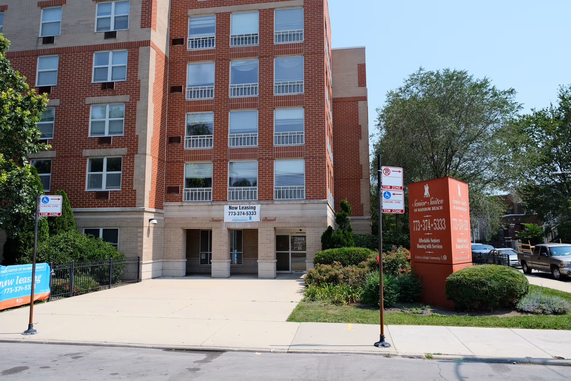 Front entrance of a multi-story brick senior living building with a red sign reading Senior Suites of Rainbow Beach.