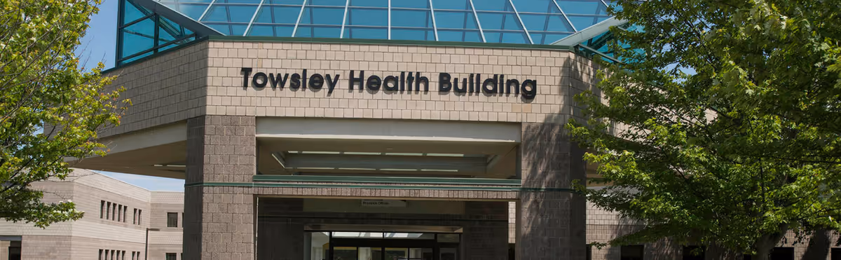Exterior view of the Towsley Health Building with a modern architectural design, surrounded by green trees under a clear blue sky.
