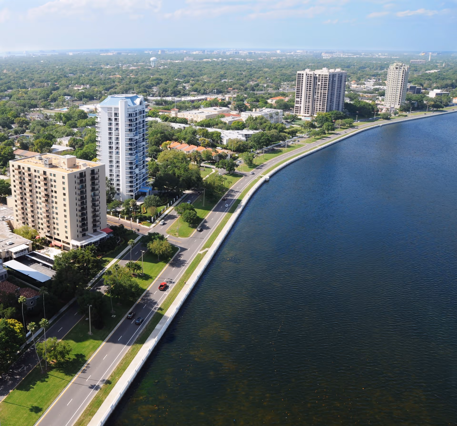 Aerial view of waterfront high-rise residential buildings along a curved seawall and adjacent road.