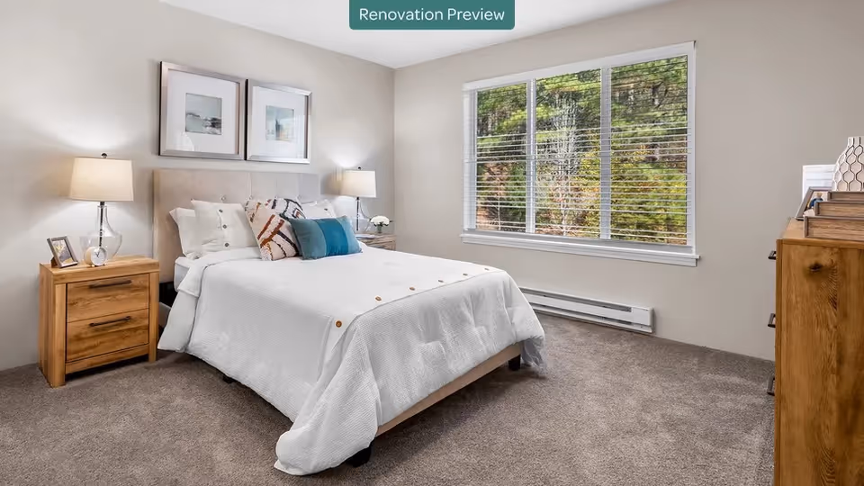 Bright furnished bedroom with a made bed, two bedside tables with lamps, a large window and carpeted floor.