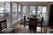 Enclosed sunroom with a square dining table and four chairs surrounded by large windows overlooking the outdoors.