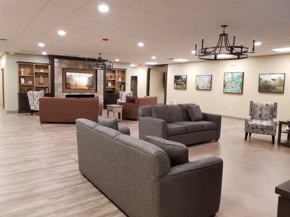 Spacious communal lounge with sofas and armchairs facing a TV and fireplace, with artwork on the walls.