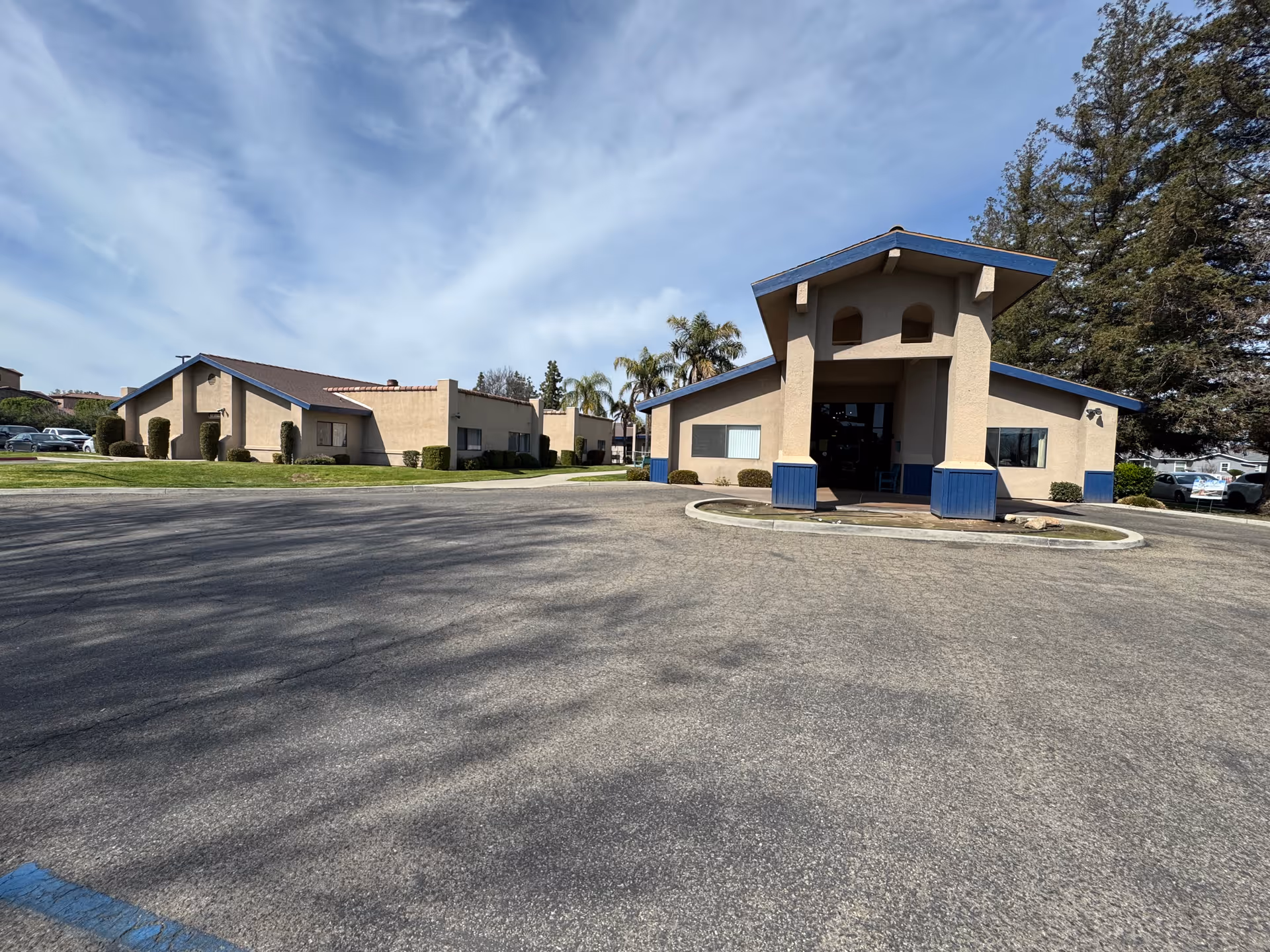 Low-rise beige senior living building with a covered entrance and circular driveway under a blue sky.