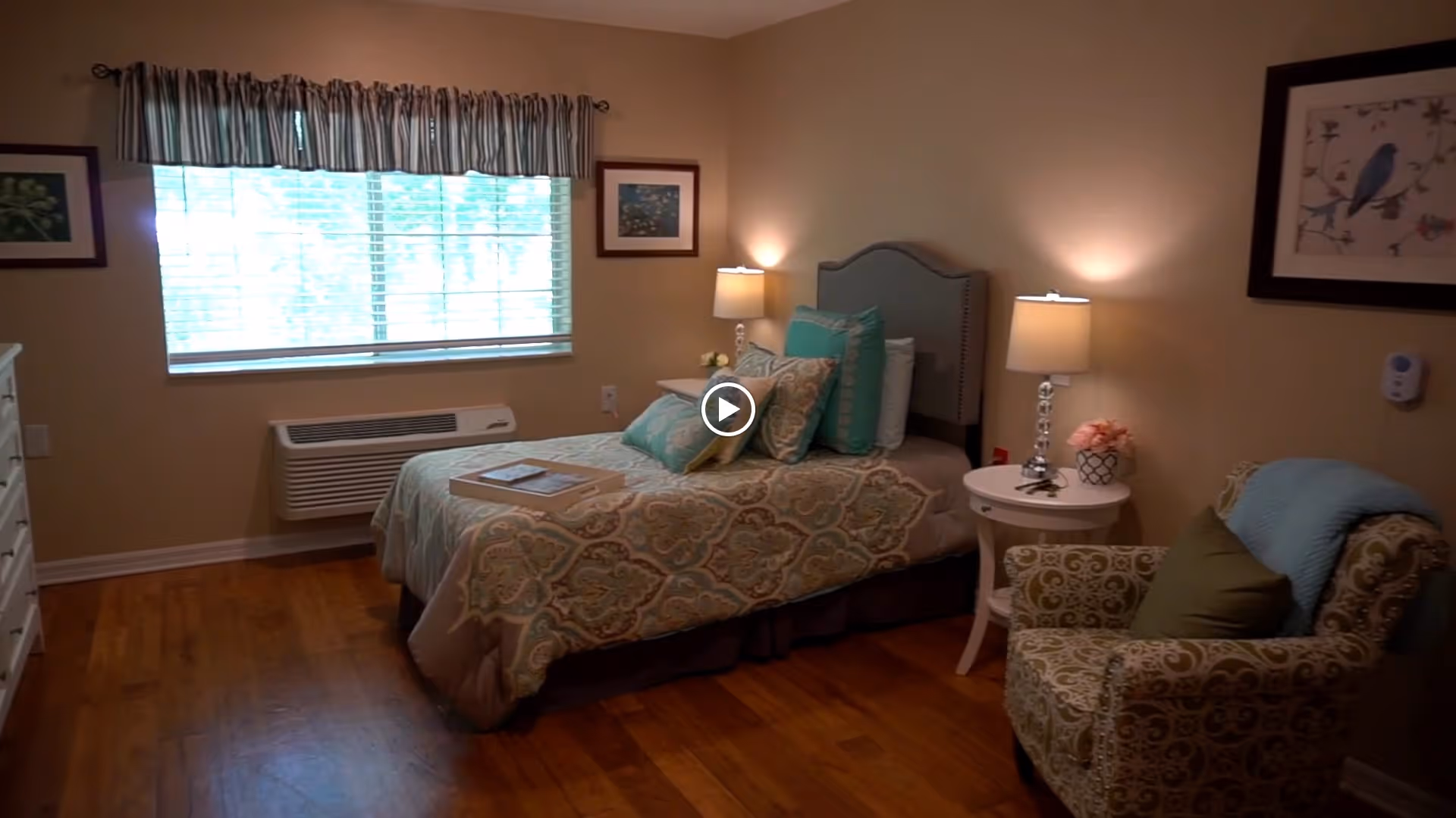 Neatly furnished bedroom with a single bed, bedside tables and lamps, an upholstered armchair and a window with blinds.