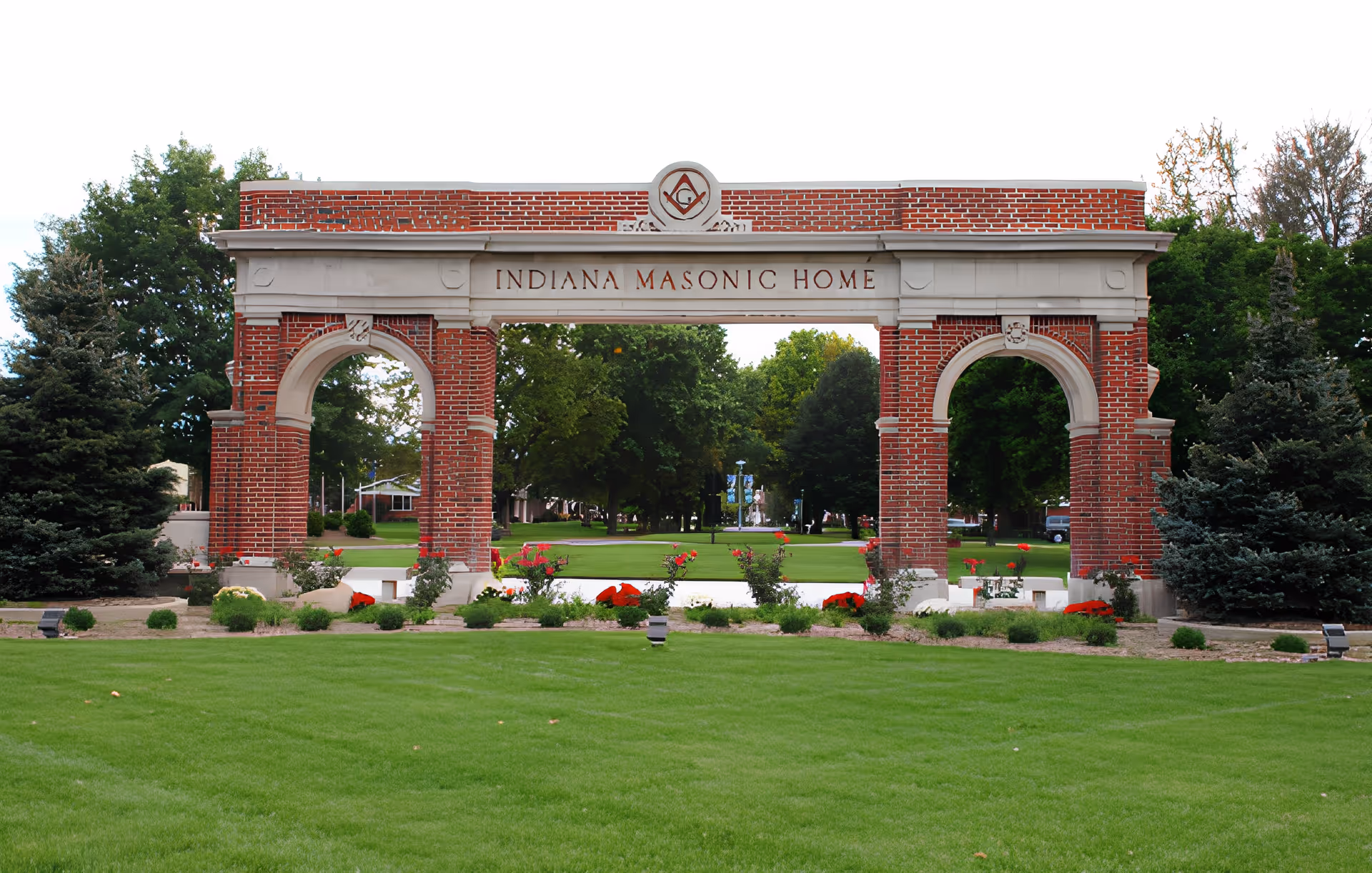 Large brick entrance arch engraved with "Indiana Masonic Home" standing before a manicured lawn and trees.