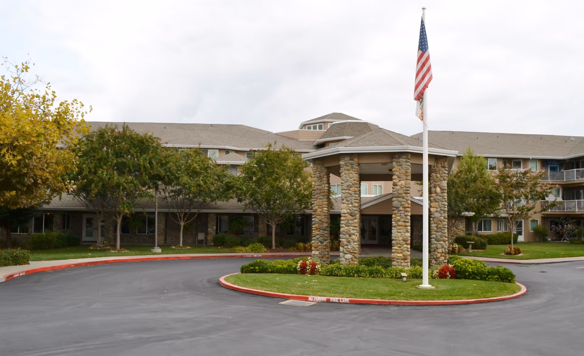 Front entrance of Creekside Oaks Retirement Community with stone pillars and flag.