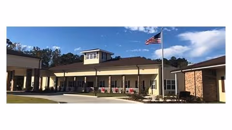 Exterior view of Ponchatoula Community Care Center building with a flagpole displaying the American flag in front, under a partly cloudy blue sky.