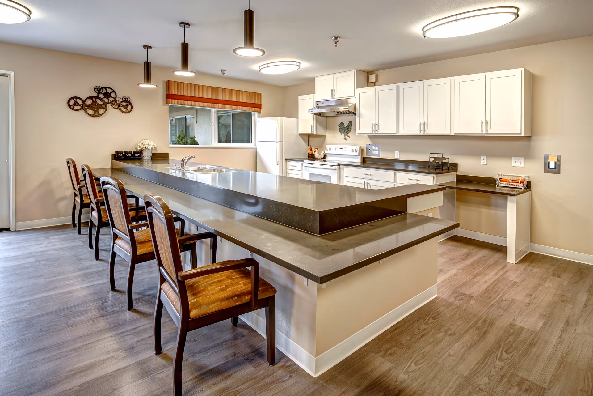 Modern communal kitchen with a long two-tier island, bar seating, white cabinets, and pendant lighting.