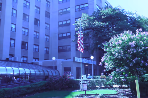 Exterior view of Clove Lakes Health Care and Rehab Center with flag, entrance, and surrounding landscaping.
