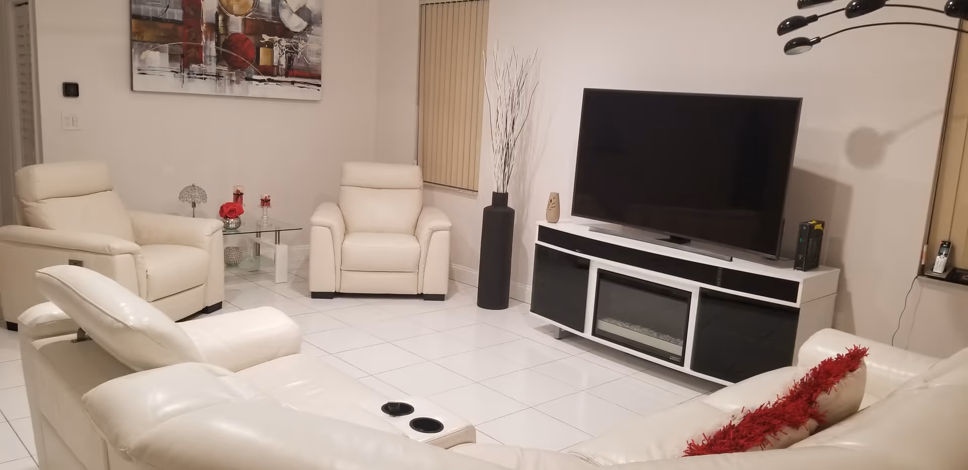 Bright modern living room with white leather sofas and recliners around a large flat-screen TV on a white media console.