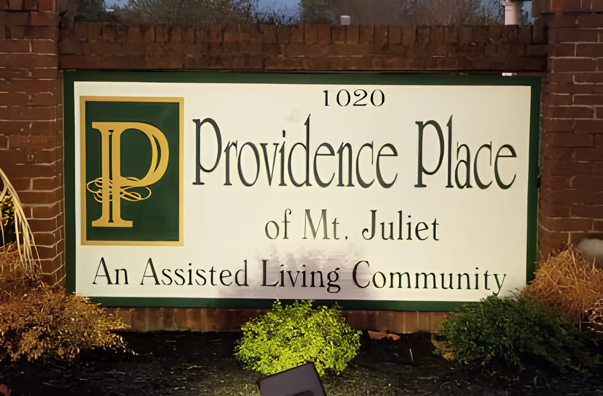 Sign for Providence Place of Mt. Juliet, an assisted living community, with the address number 1020 displayed above the name. The sign is framed by brick pillars and surrounded by small bushes.