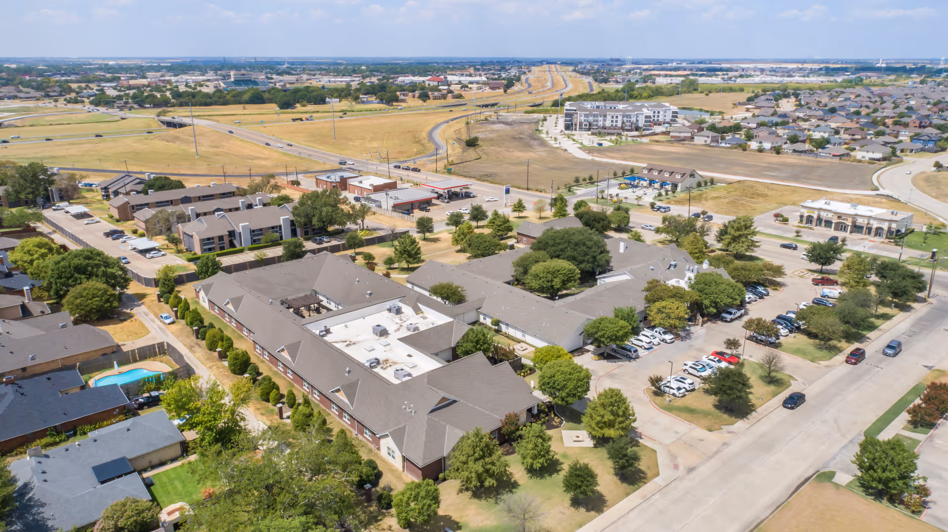 Aerial view of Brookdale Waxahachie senior living facility showing multiple connected buildings with parking lots, surrounded by trees and nearby residential neighborhoods under a clear sky.