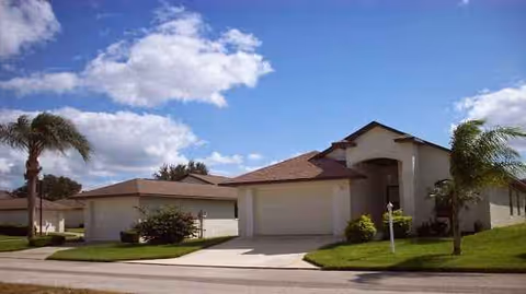 Senior living facility exterior with garages, a driveway, palm trees, and blue sky.