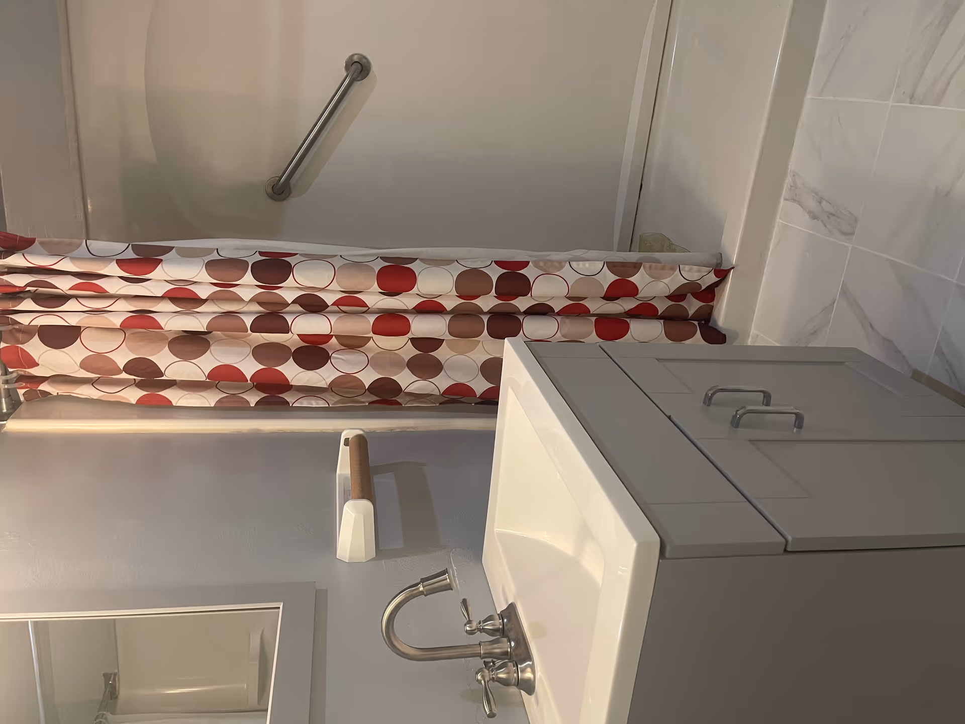 Small bathroom showing sink, countertop, faucet, and shower with red patterned curtain.