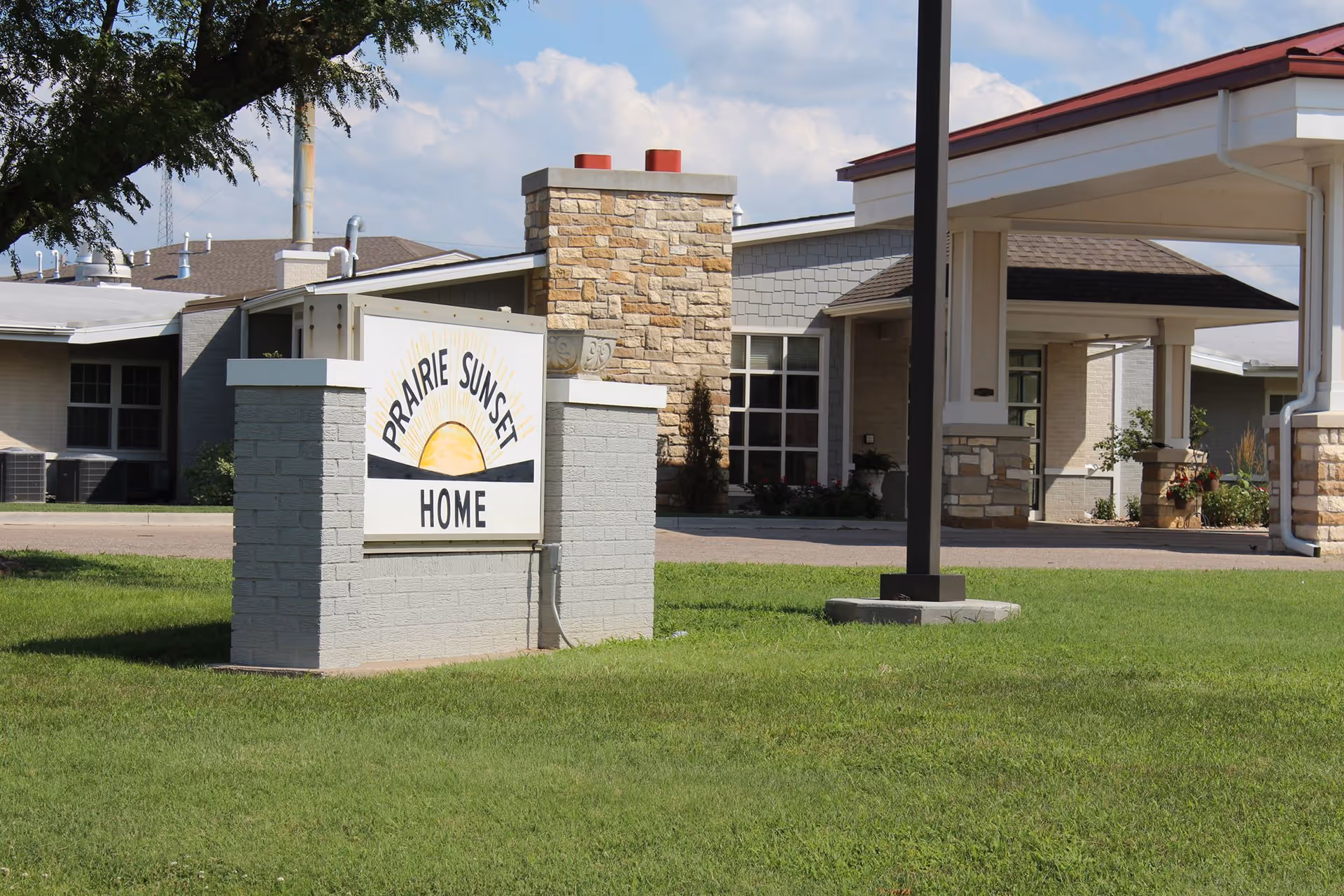 Front exterior of Prairie Sunset Home with a sign on a grassy lawn and the facility entrance in the background.