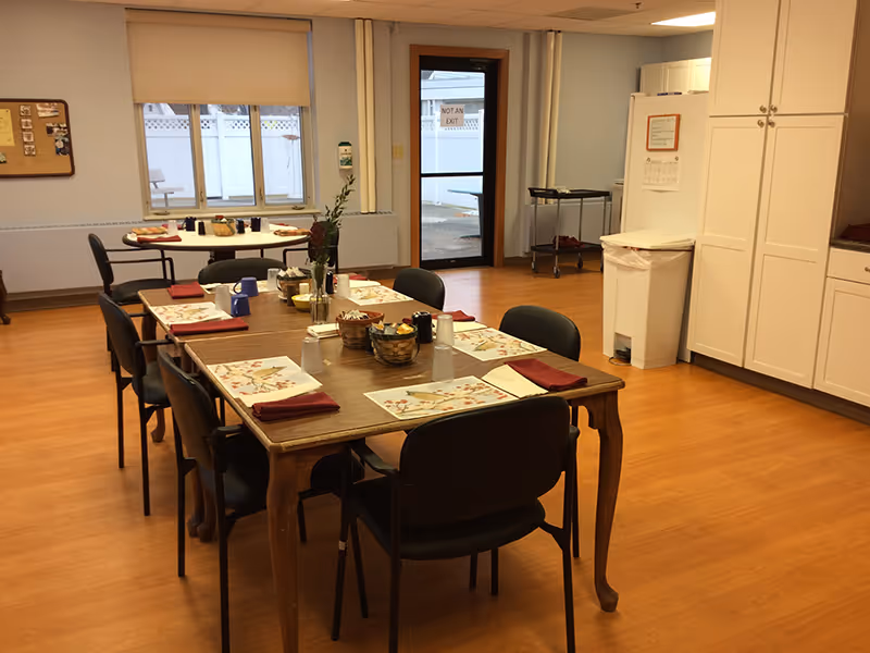 A dining room with a wooden table set with placemats and chairs, cabinets, and a door to the outside.