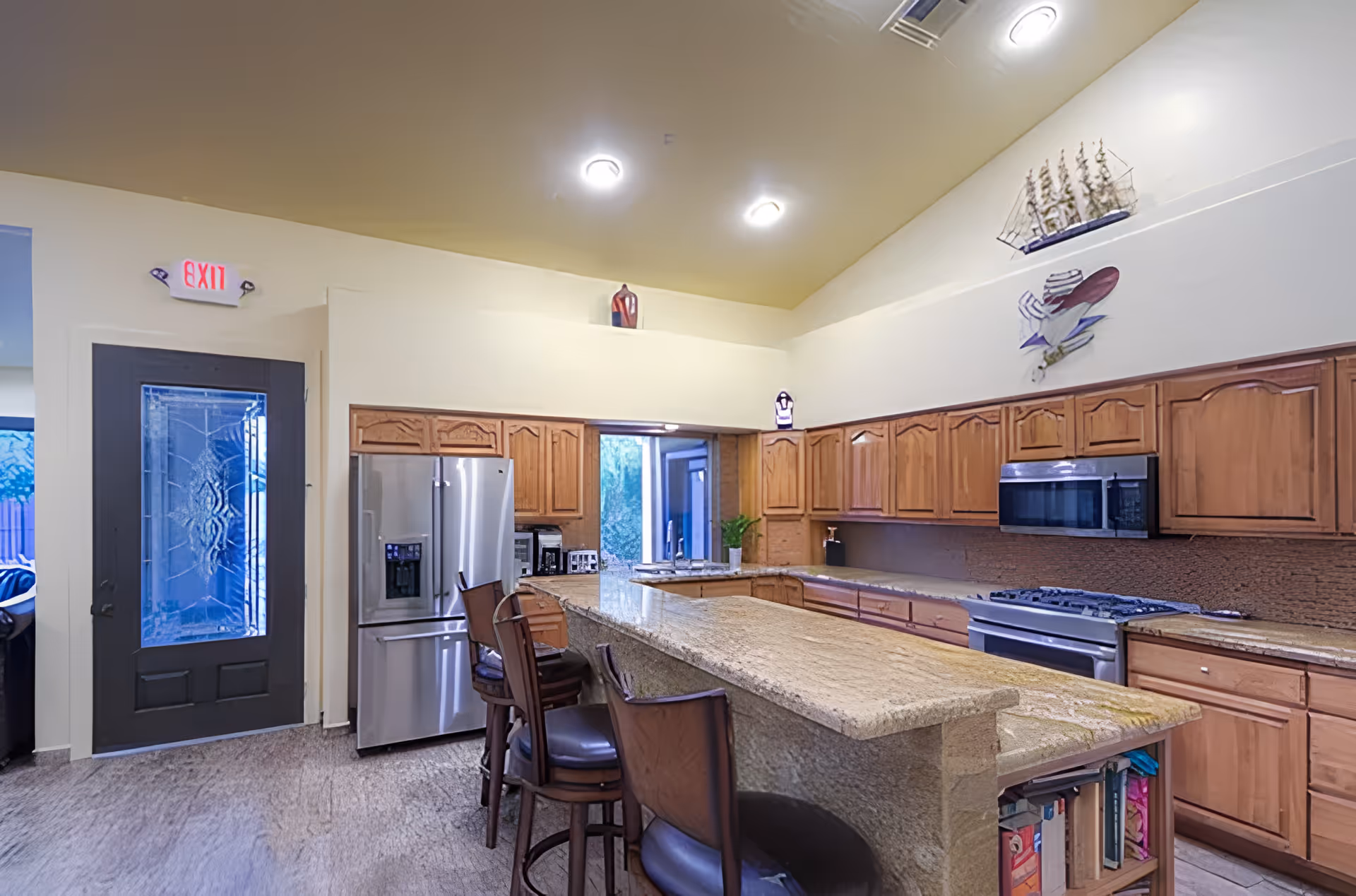 Spacious kitchen with a long granite island, wooden cabinets, stainless steel refrigerator and stove, and bar stools.