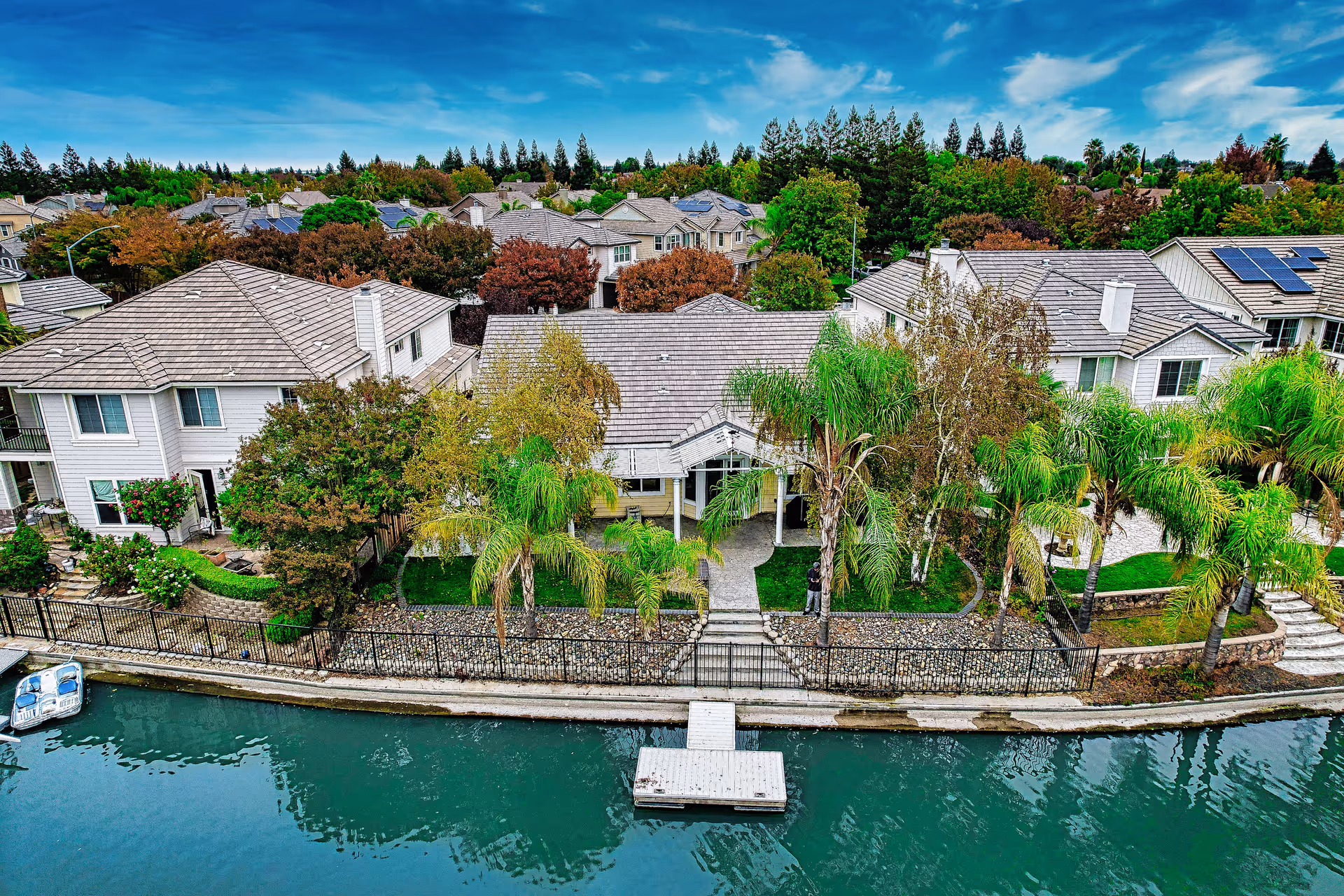 Aerial view of a waterfront residential building and neighboring homes with palm trees and a small dock.