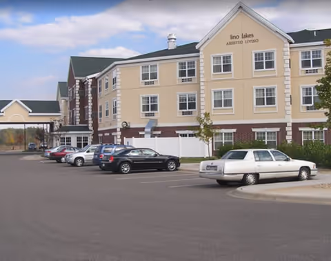 Exterior view of Lino Lakes Assisted Living building with parked cars in front.