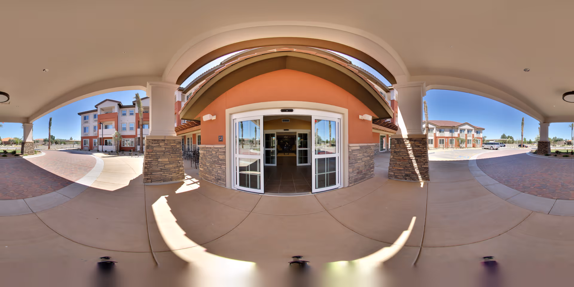 Covered main entrance with automatic sliding glass doors under an arched portico leading into a multi-story senior living building.