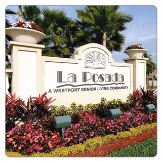 Entrance sign for La Posada, a Westport senior living community, surrounded by colorful flowers and palm trees under a clear sky.