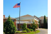 Sunny day exterior of The Manor & Villages building with flagpole and welcoming entrance.