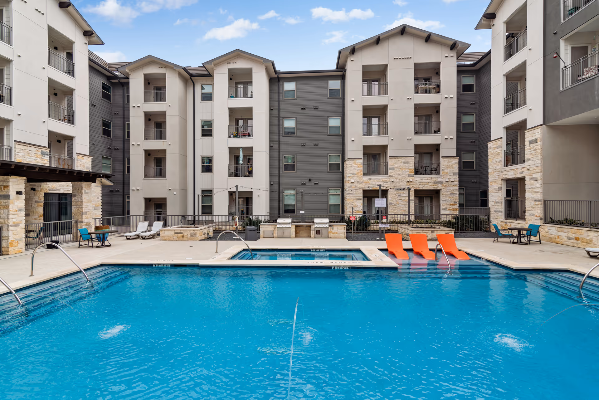 Outdoor courtyard with a swimming pool, orange lounge chairs and a multi-story apartment building behind it.