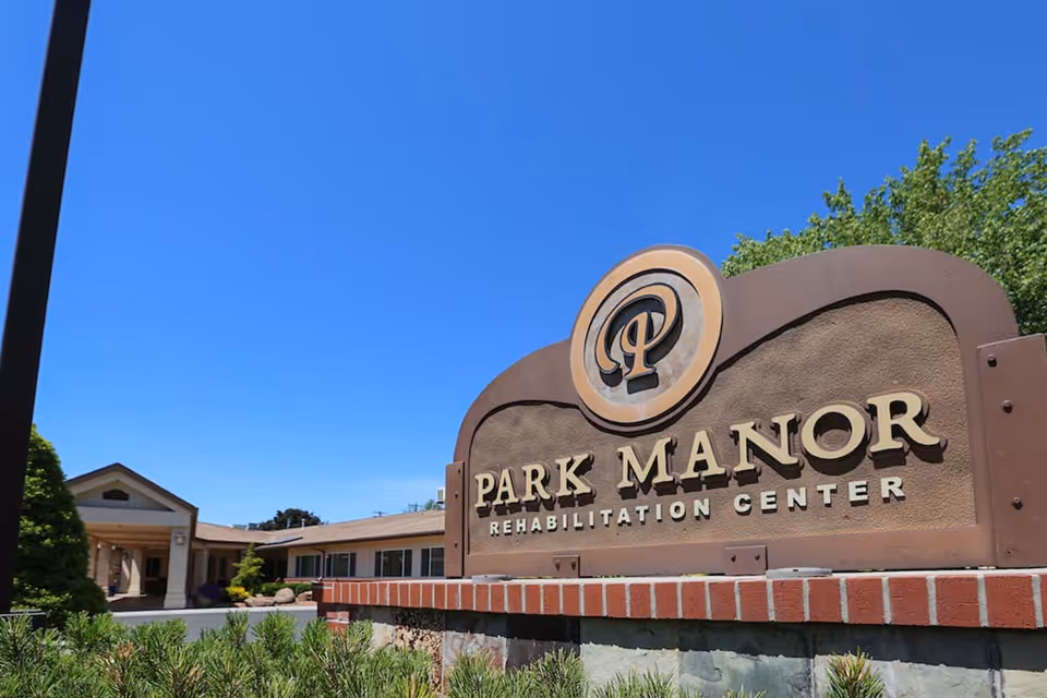 Outdoor view of the entrance sign for Park Manor Rehabilitation Center with a clear blue sky and part of the building visible in the background.